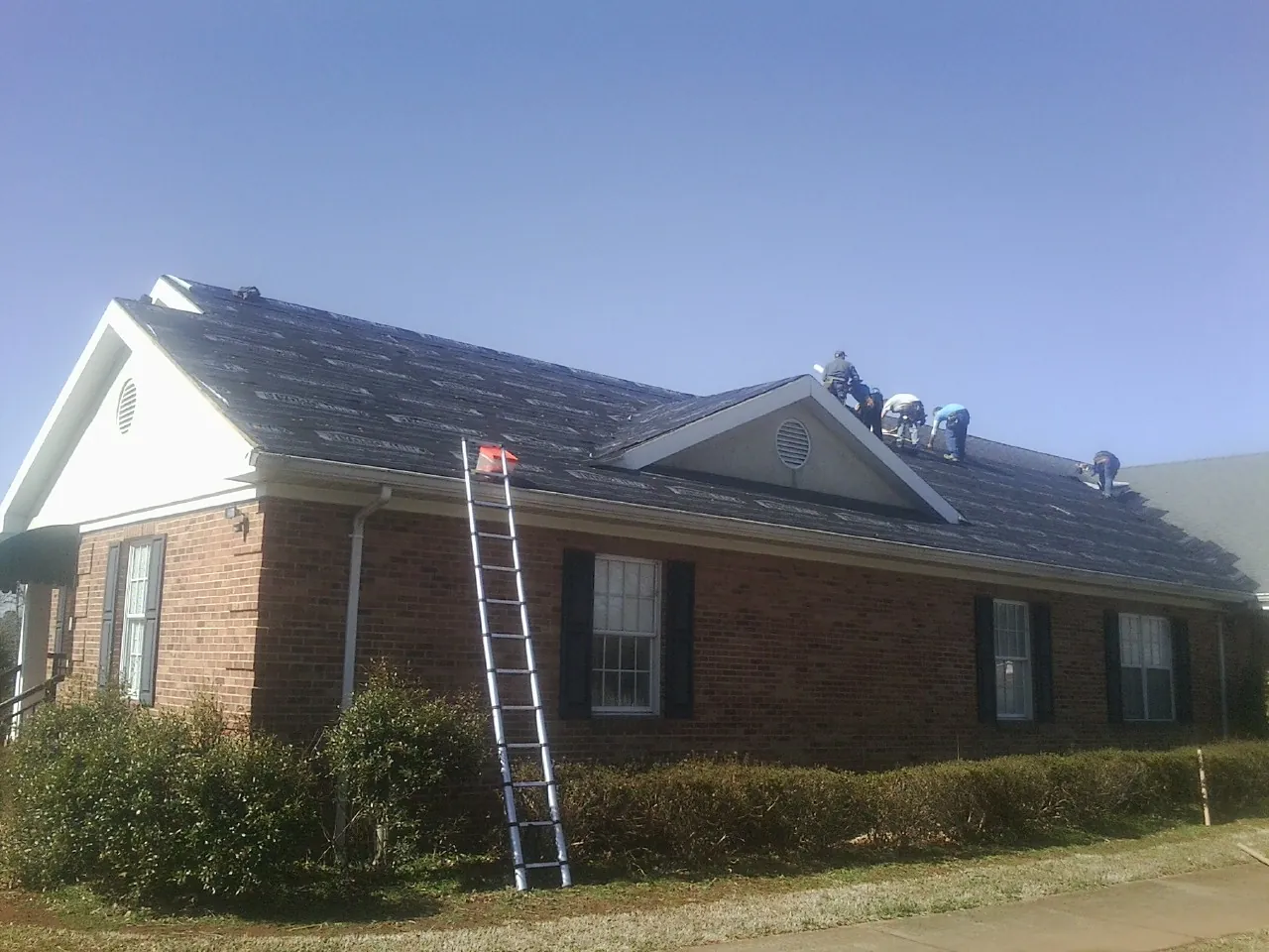 Crew tearing shingles off a brick ranch roof with a ladder set — Emergency Roof Repair work by our crew in Chester Heights