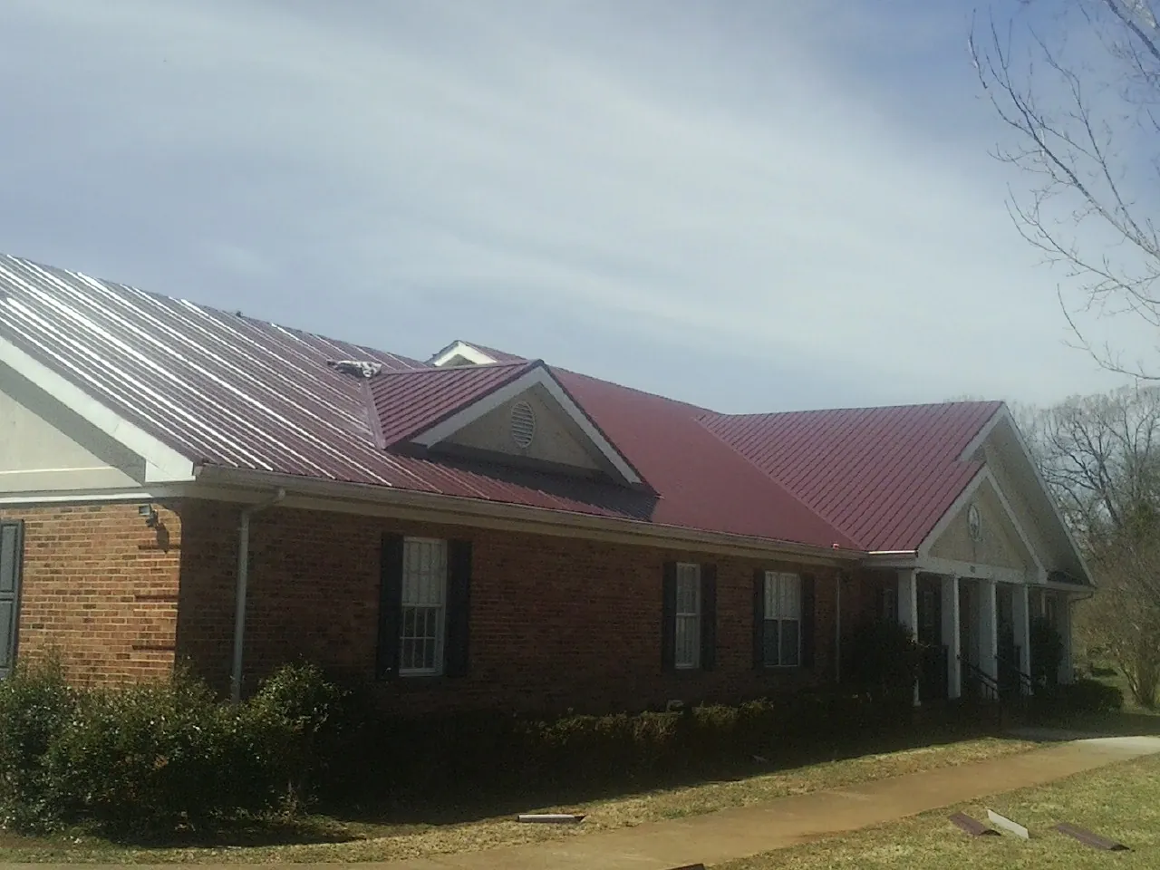 Red metal roof with gabled entries on a long brick building, from a Hail Damage Roof Repair job in Chester Heights