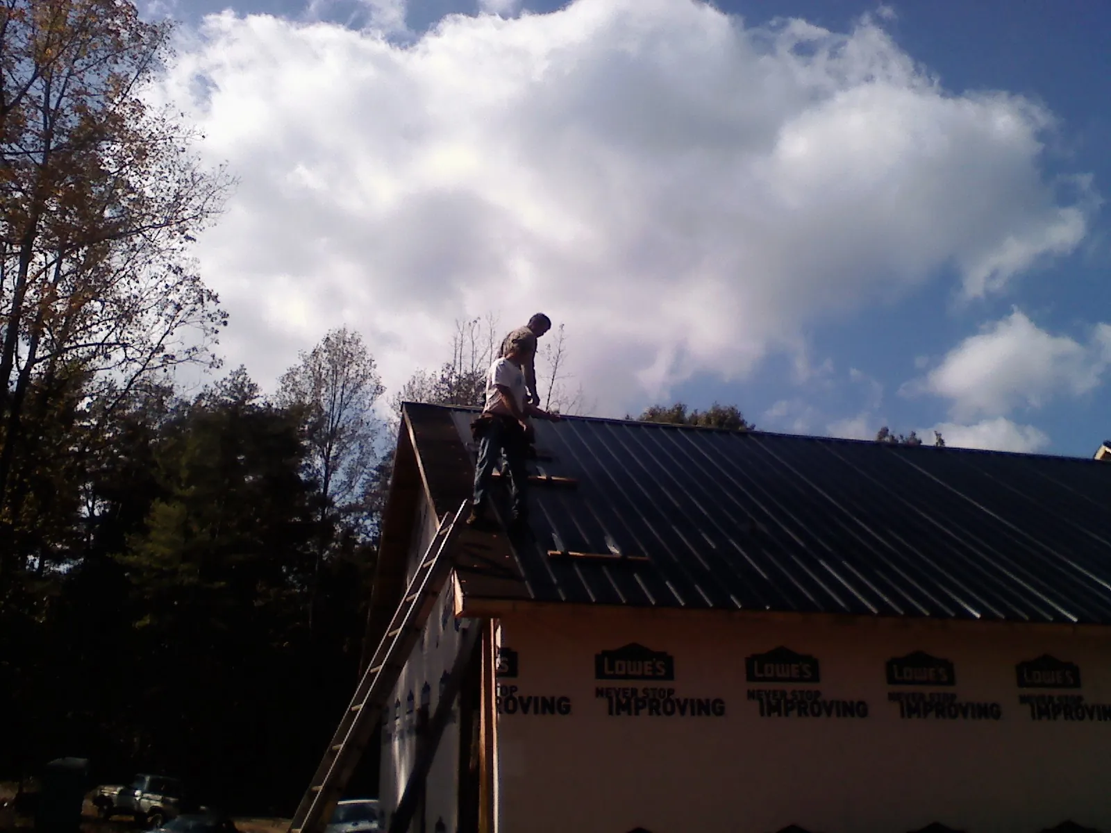 Roofer fastening dark metal panels high against a cloudy sky, from a Roof Inspection job in Chester Heights