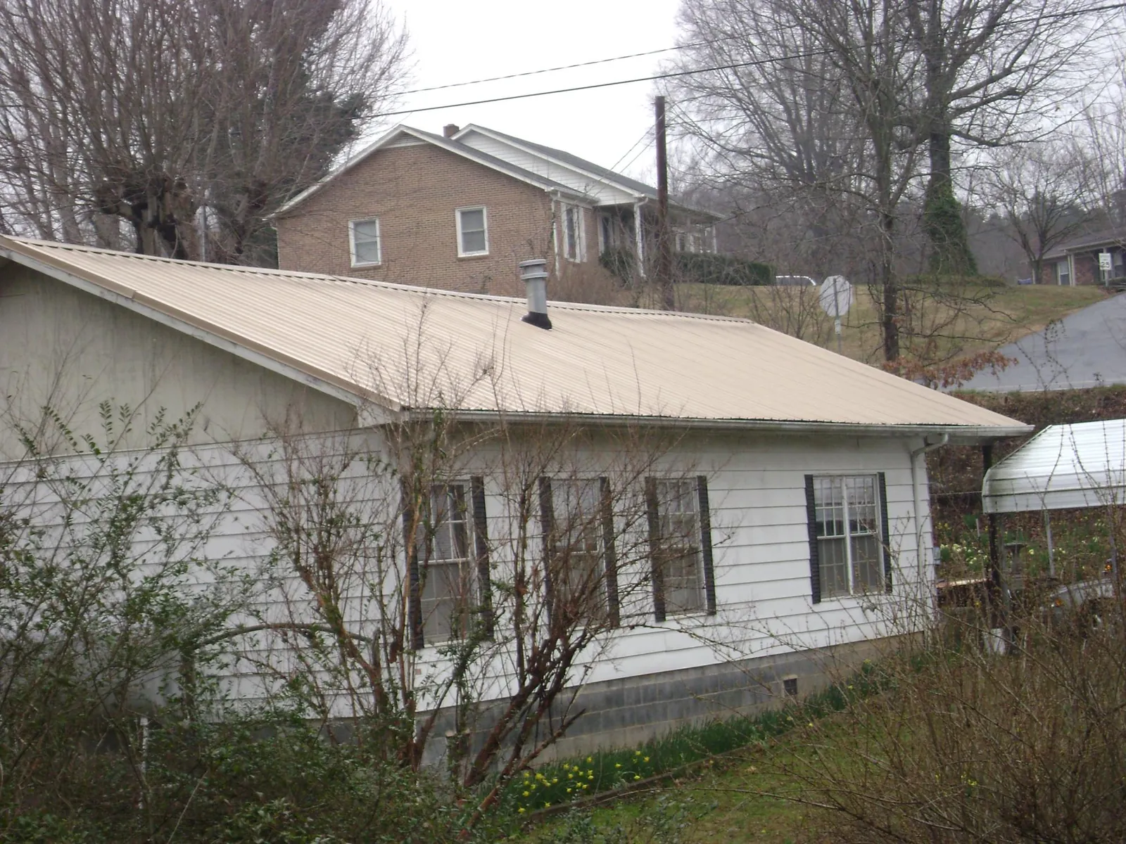 Tan metal roof on a white sided house set into a hillside — Commercial Roofing by Roofing Brothers in Chester Heights